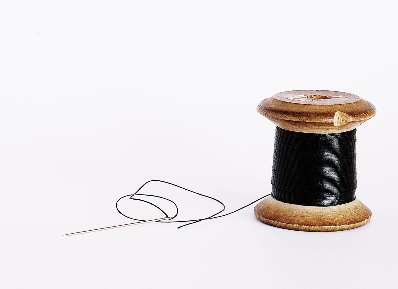 Mastering the First Impression: Your intriguing post title goes here Close-up of a wooden spool with black thread and a sewing needle on a white background.