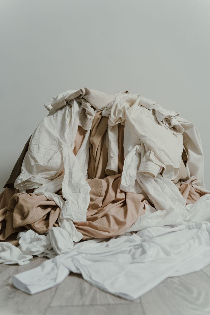 Home A heap of beige and white clothes casually piled on a wooden floor.